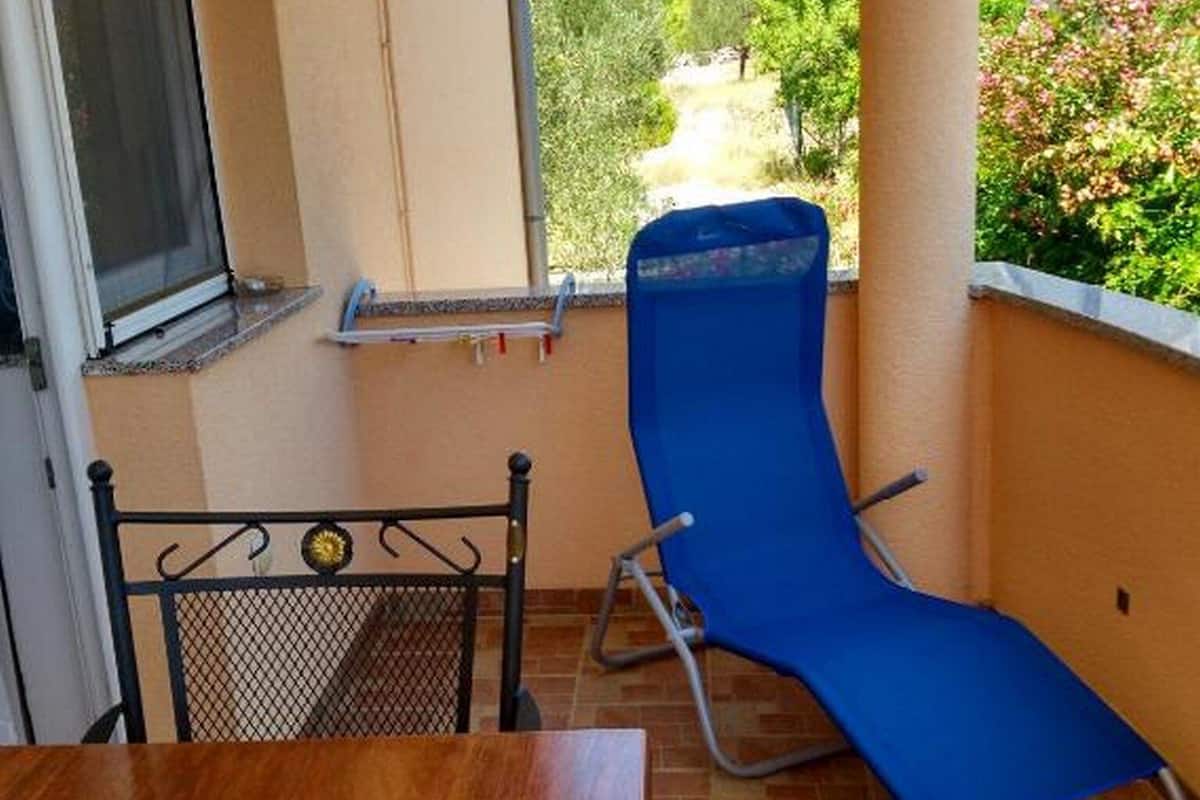 Un balcon avec un fauteuil de jardin bleu, une table en bois et une chaise en métal.