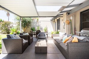 Un patio al aire libre con mobiliario de mimbre, una parrilla y plantas en macetas.