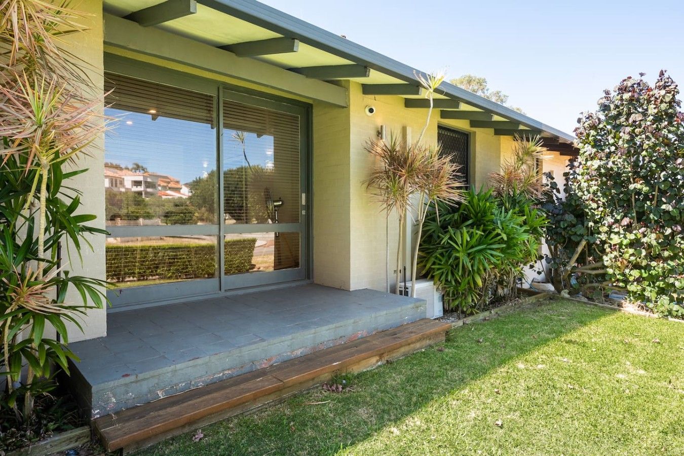 A modern house with a covered porch, sliding glass doors, and a well-maintained garden.