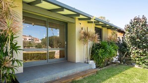 Ein modernes Haus mit überdachter Veranda, Schiebegläsern und einem gepflegten Garten.