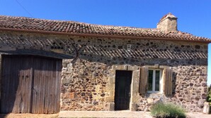 Un edificio rústico de piedra con techo de tejas, una puerta de madera y una ventana pequeña con contraventanas.