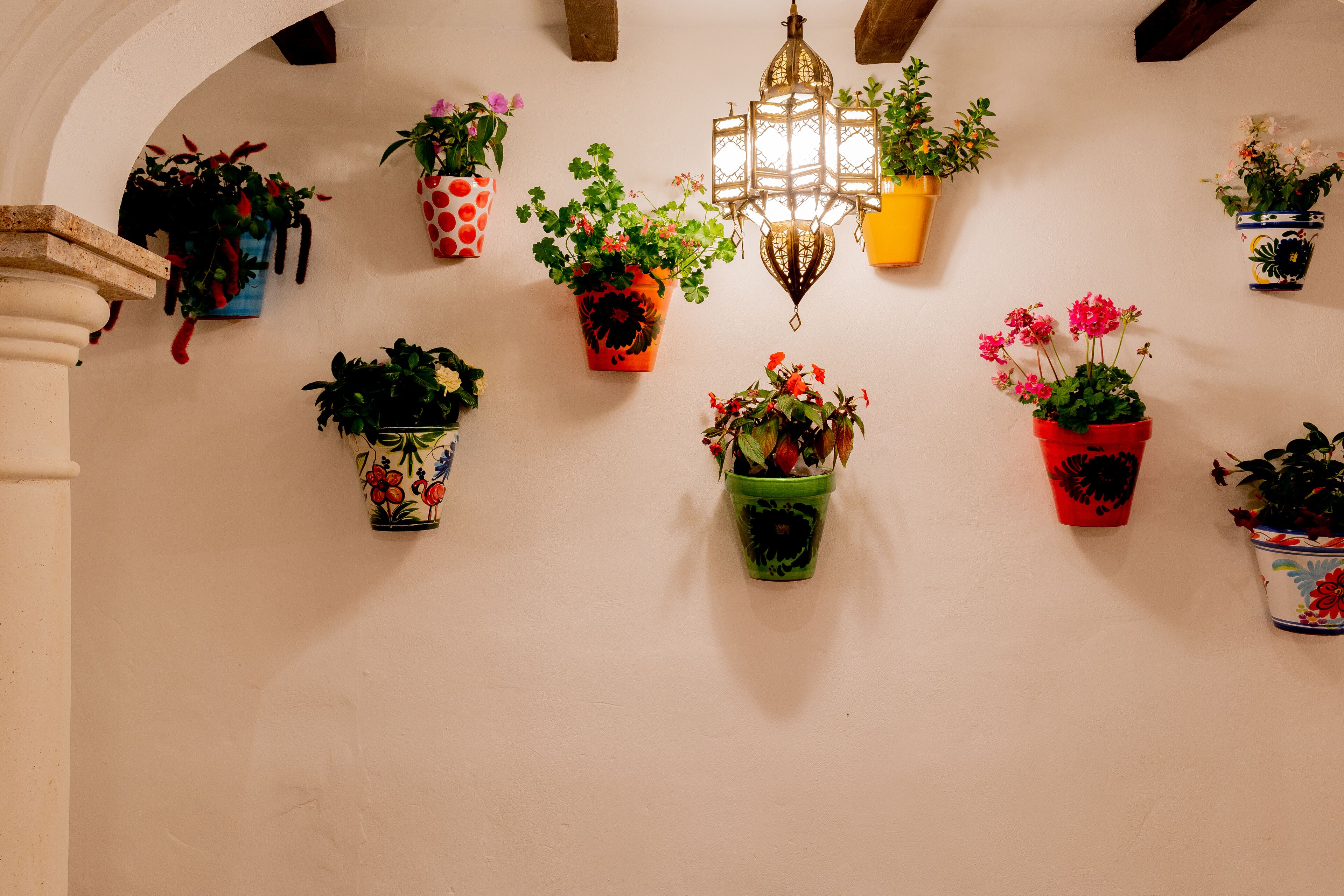 A hallway with multiple potted plants hanging on the wall, a decorative lantern, and a stone column.
