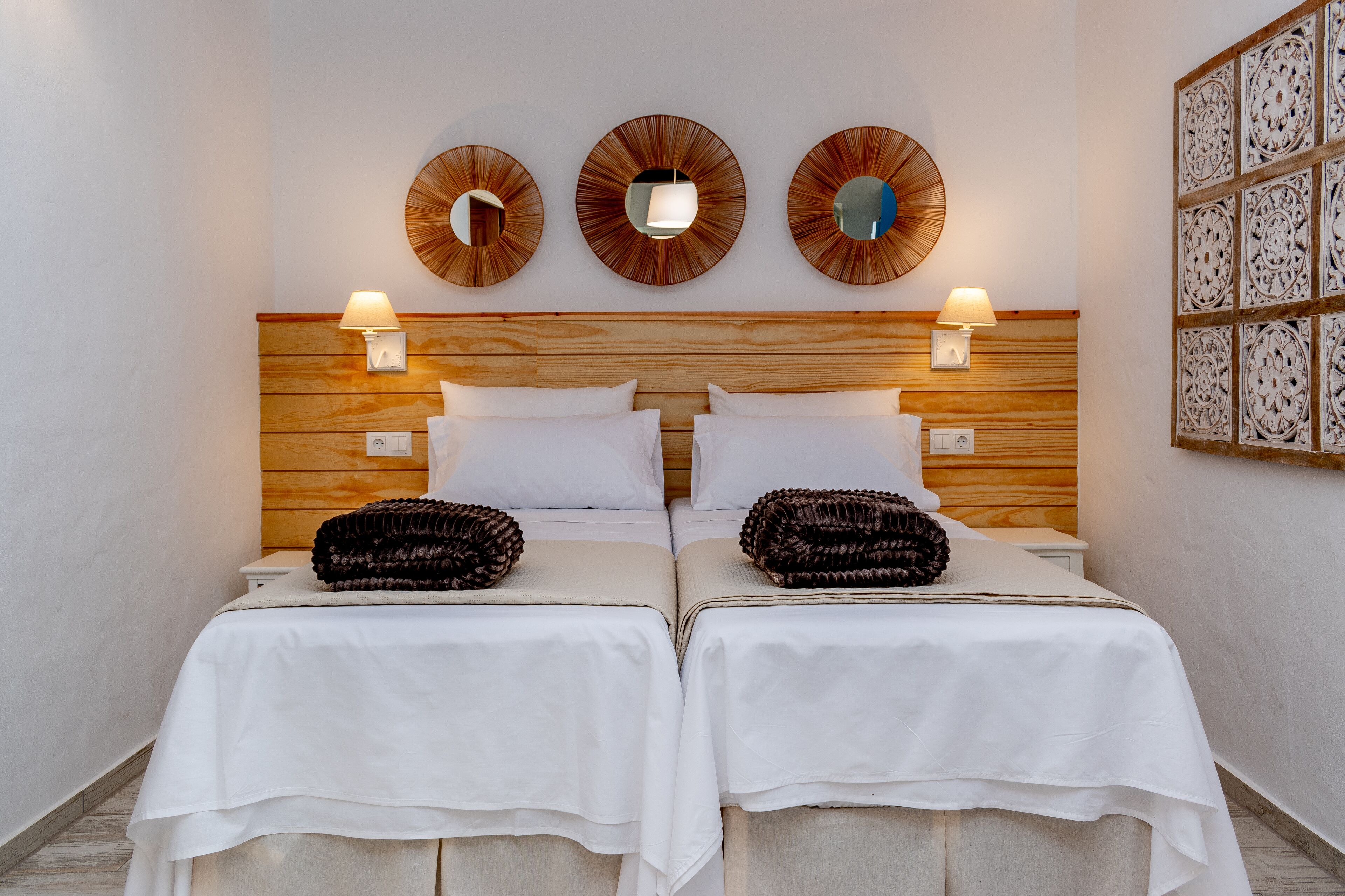 Een tweepersoonskamer met twee bedden, een houten hoofdbord, wandlampen en decoratieve spiegels.