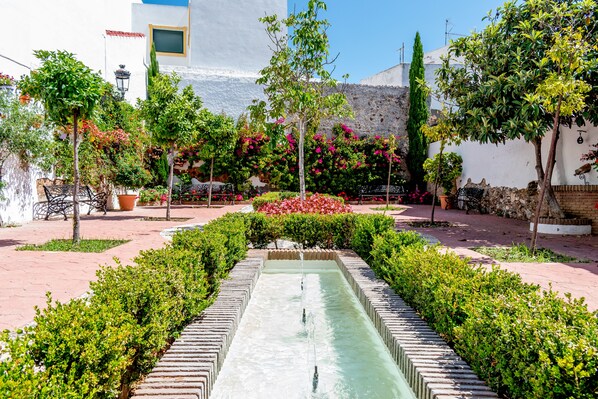 A courtyard with a central water feature, surrounded by neatly trimmed hedges and flowering plants. - Casa del Patio - Boutique Apartments (Estepona)