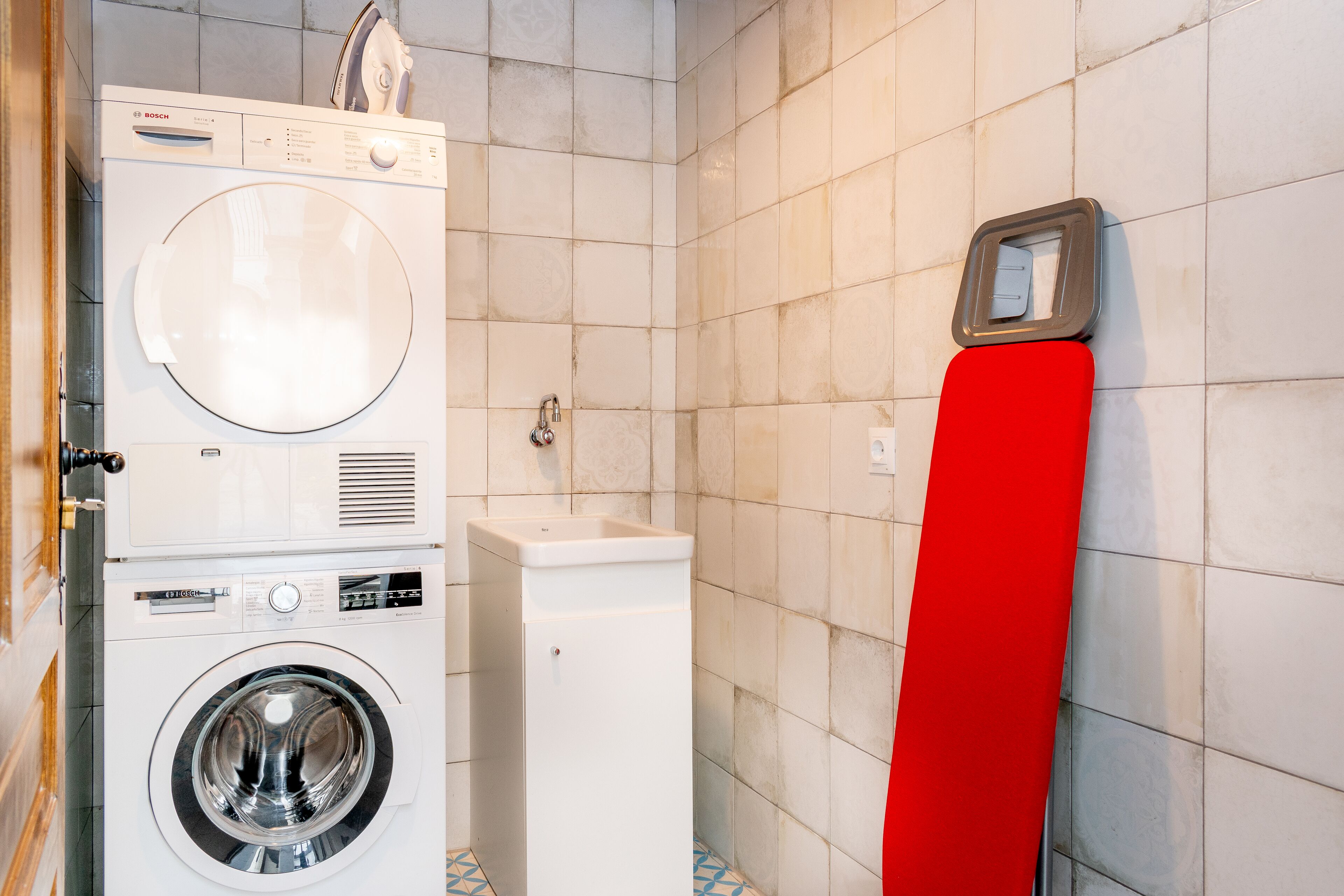 A compact laundry area with a Bosch washing machine and dryer, a sink, and a red towel rack.