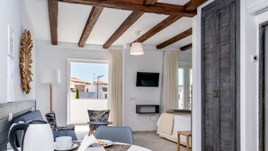A modern hotel room with a dining area, a TV, and a large window with a view of buildings. - Casa del Patio - Boutique Apartments (Estepona)