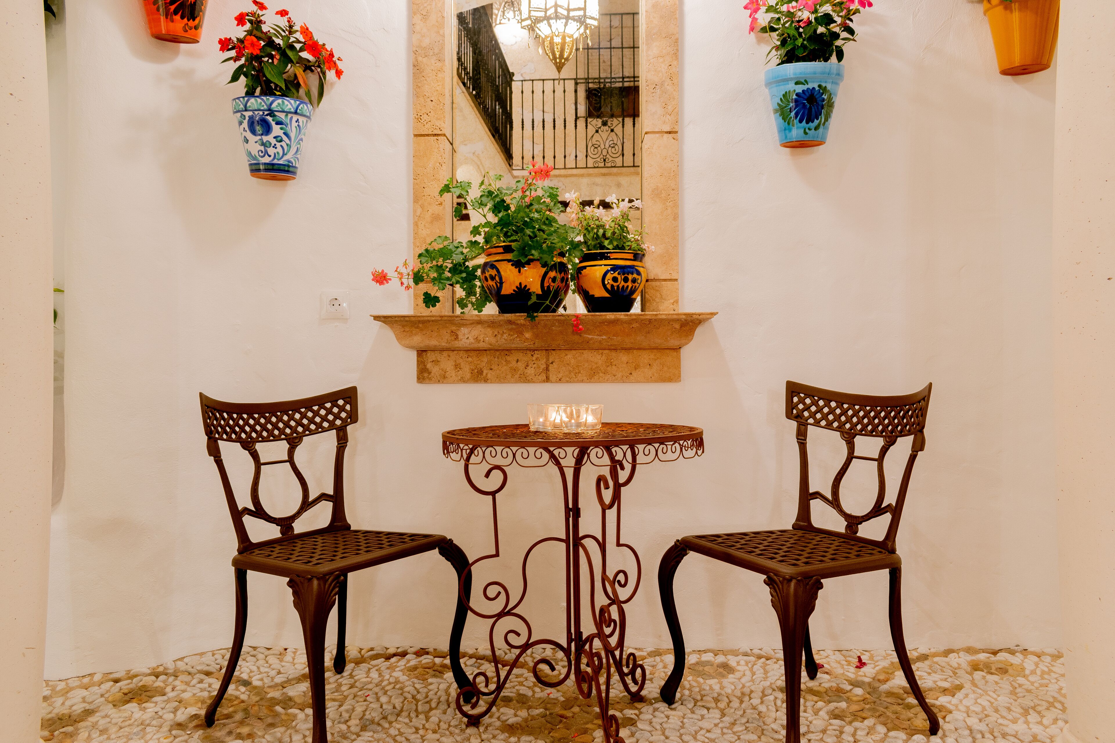 Une petite table avec deux chaises, une bougie et des plantes en pot, le tout placé devant un mur blanc.