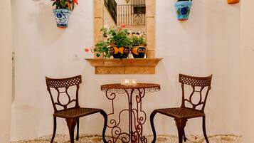 Une petite table avec deux chaises, une bougie et des plantes en pot, le tout placé devant un mur blanc.