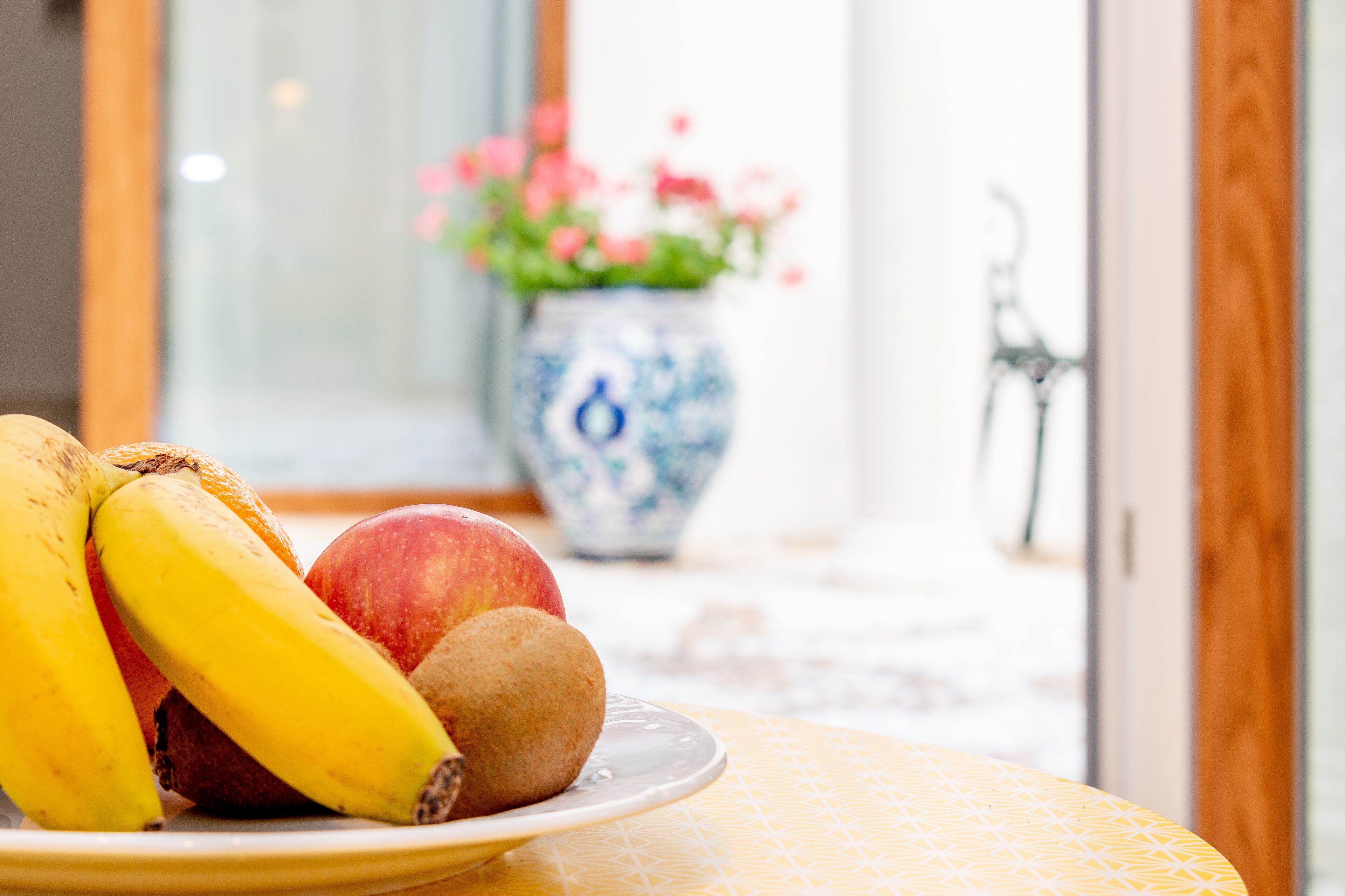 A plate with bananas, an apple, and a kiwi on a yellow tablecloth.