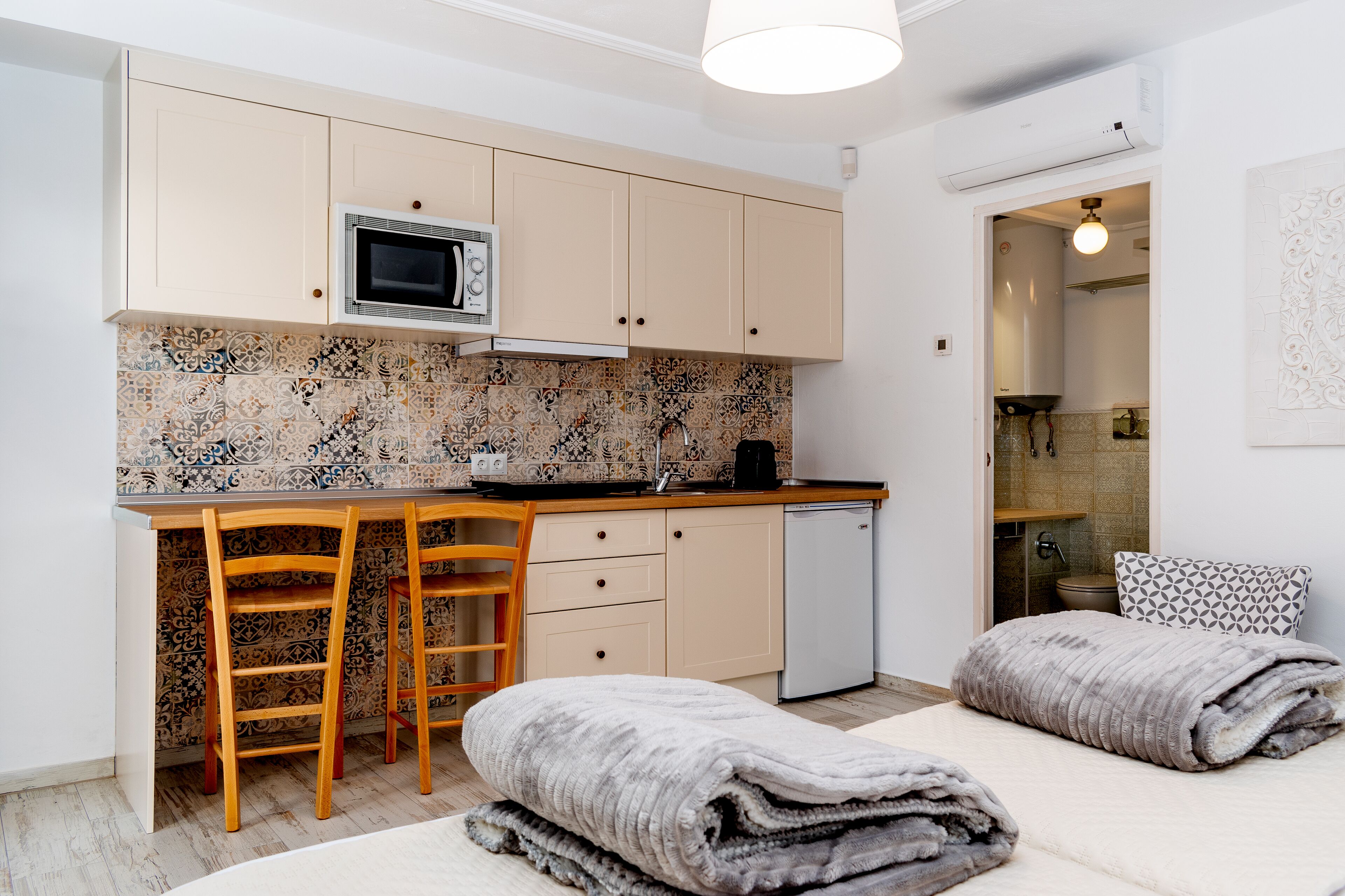 Una cocina compacta con microondas, dos taburetes tipo barra, lavavajillas y un salpicadero decorado.