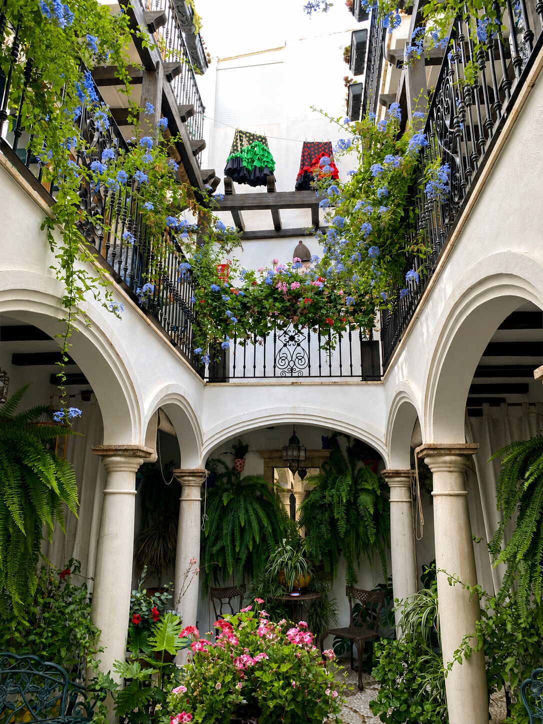 Un patio con arcos, un balcón con plantas y ropa tendida.