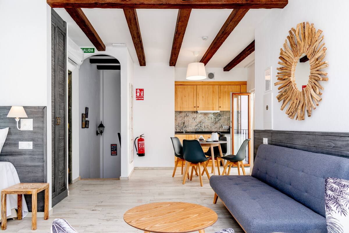 A modern living room with a sofa, a round wooden table, and a dining area with chairs and a kitchen in the background.