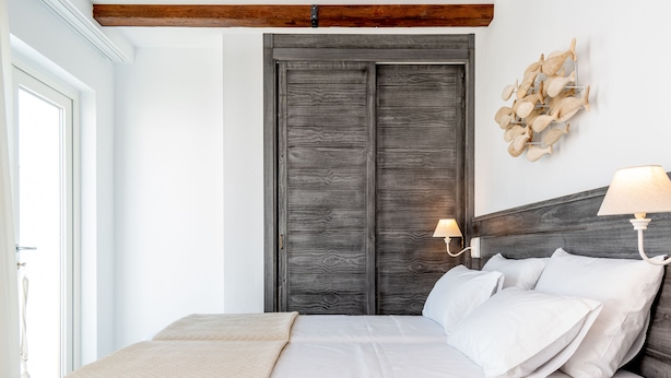 A bedroom with a large bed, a wooden headboard, a wall-mounted light fixture, and a decorative wall piece. - Casa del Patio - Boutique Apartments (Estepona)