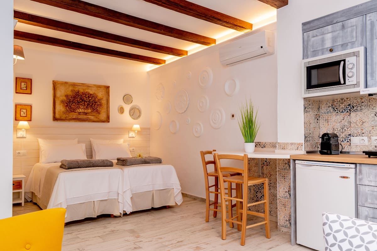 A modern bedroom with two beds, a small dining area, and a kitchenette with a microwave and coffee maker.