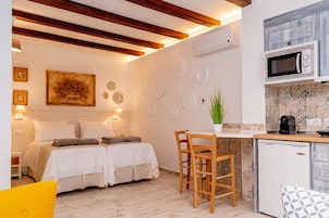 Un dormitorio moderno con dos camas, un pequeño comedor y una kitchenette con microondas y cafetera.