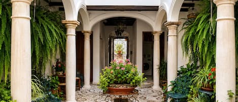 A courtyard with columns, potted plants, and a tiled floor.