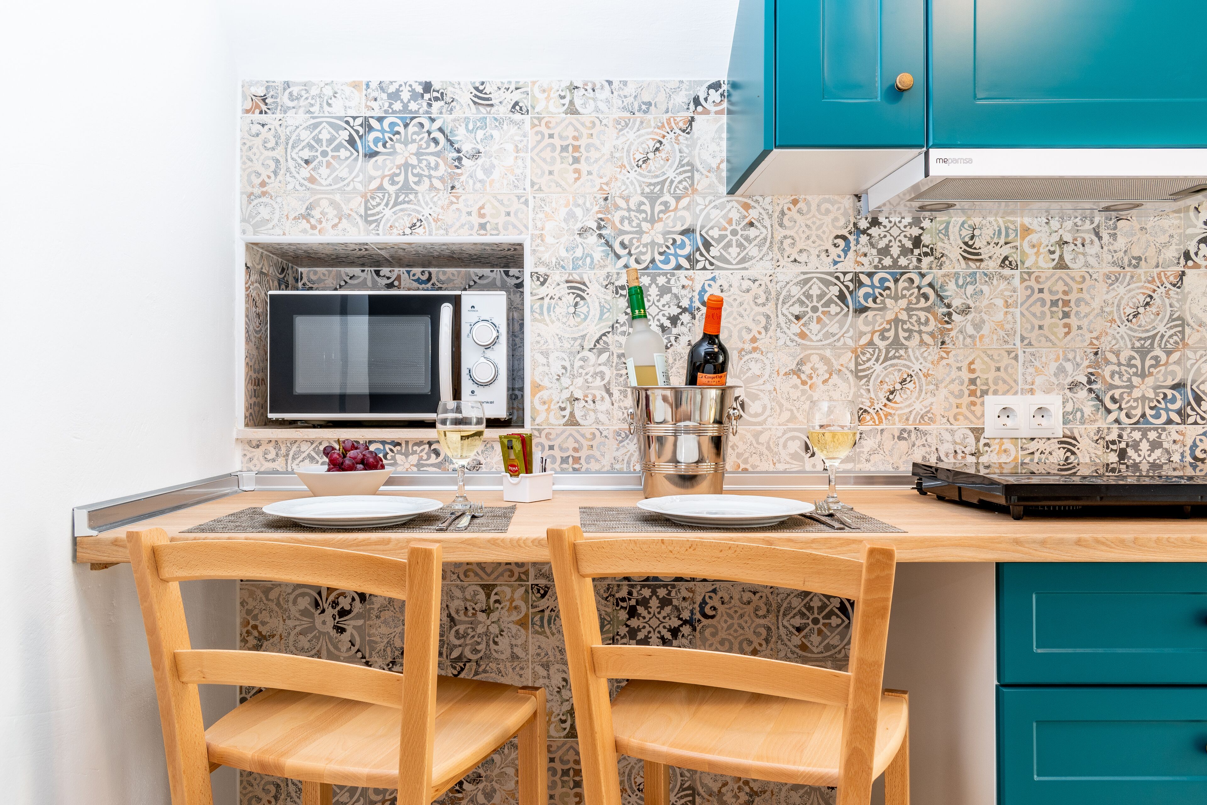 Una cocina con microondas, dos sillas, una mesa preparada para dos personas y un armario color esmeralda.