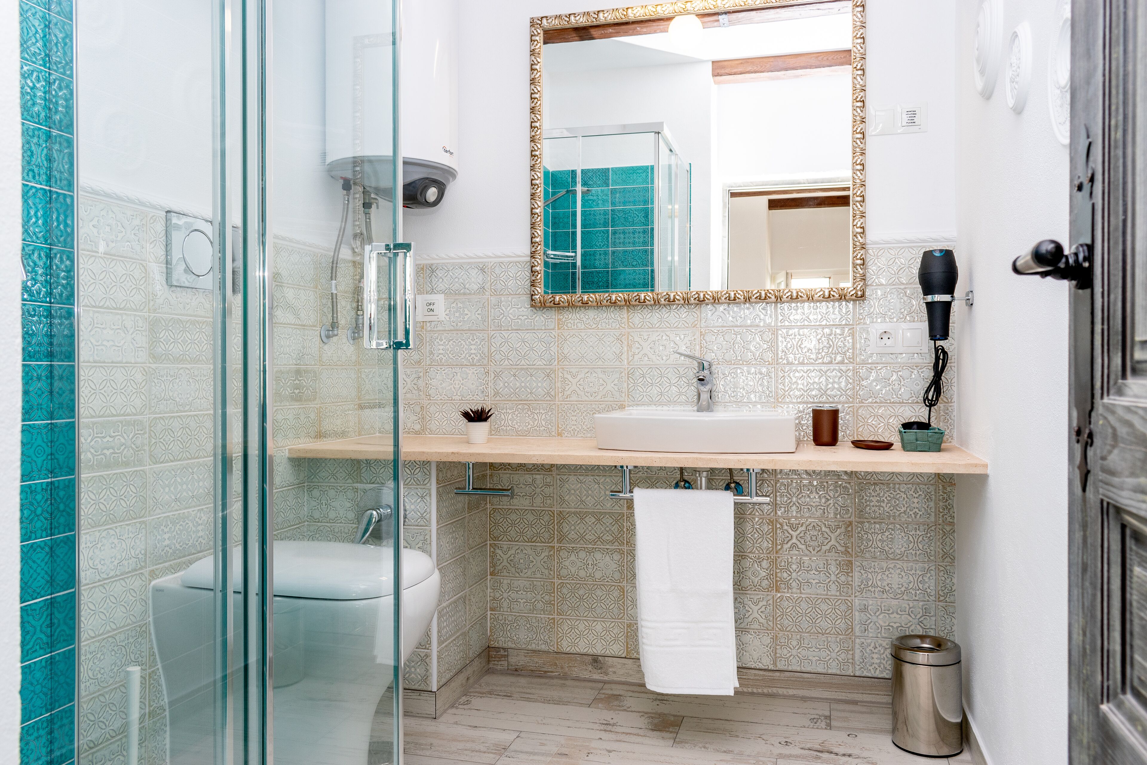 Un baño con cabina de ducha de vidrio, un lavabo con una toalla colgada y un secador de pelo en la pared.