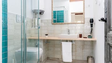 Un baño con cabina de ducha de vidrio, un lavabo con una toalla colgada y un secador de pelo en la pared.