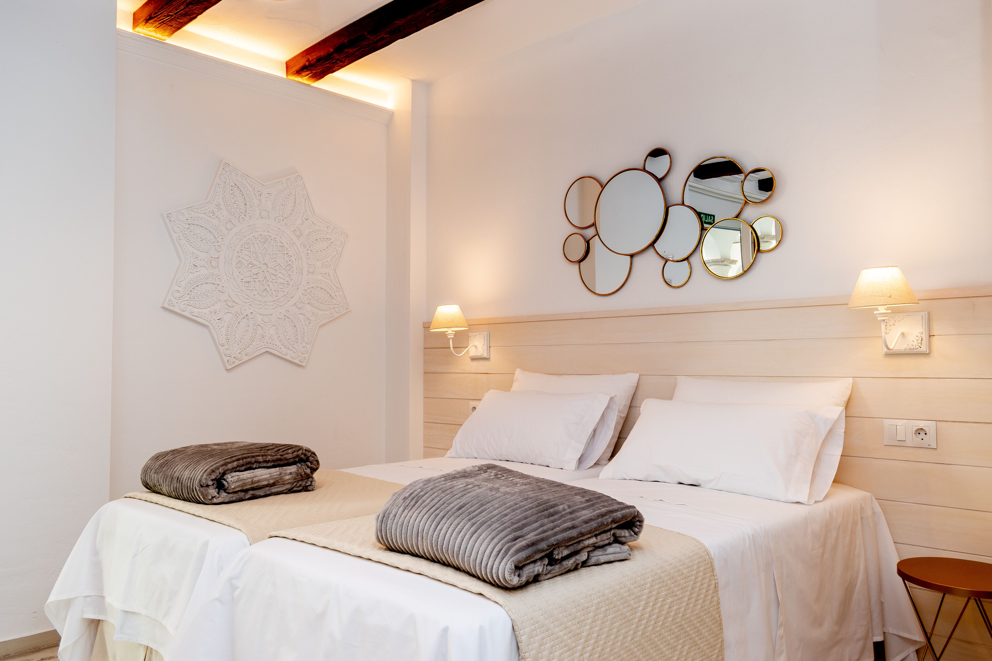 Een hotelkamer met twee bedden, een decoratief wandobject en wandlampen.