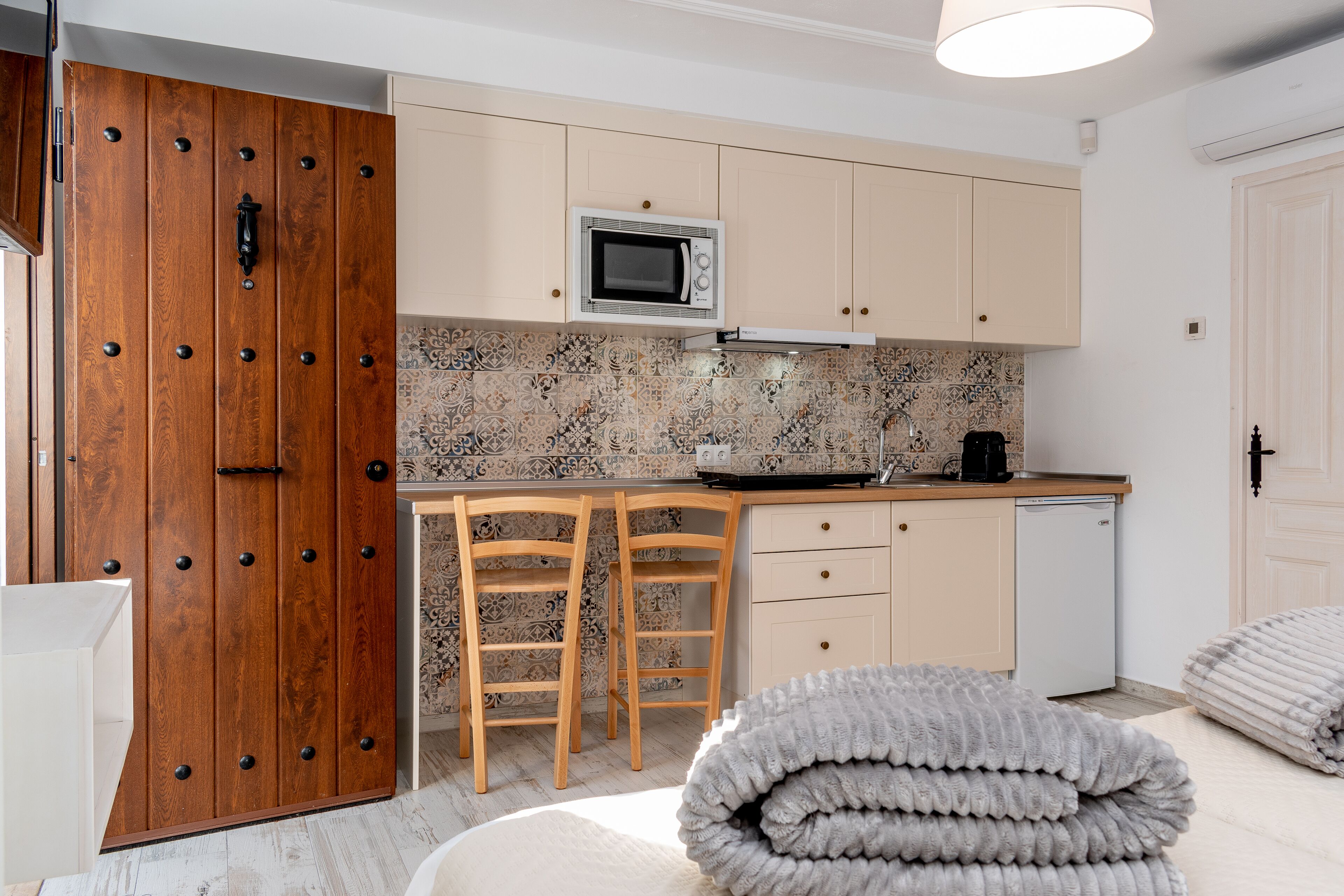 A compact kitchen with a microwave, two wooden chairs, a small table, and a white door.