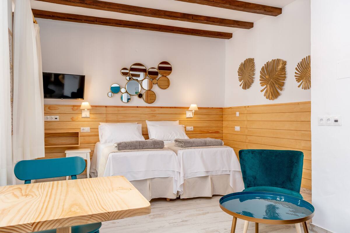 A hotel room with two beds, a TV, wooden paneling, and a teal chair.