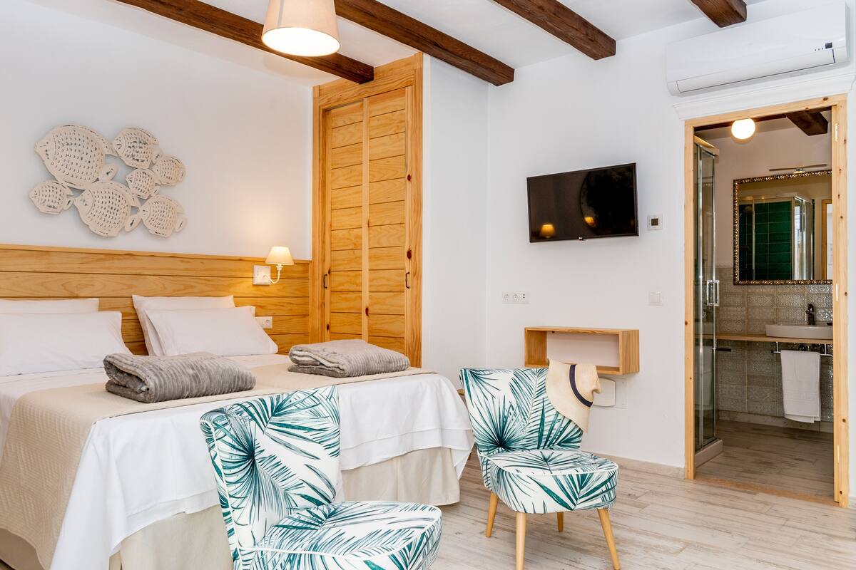 A bedroom with a bed, two chairs, a TV, and a bathroom visible through an open door.