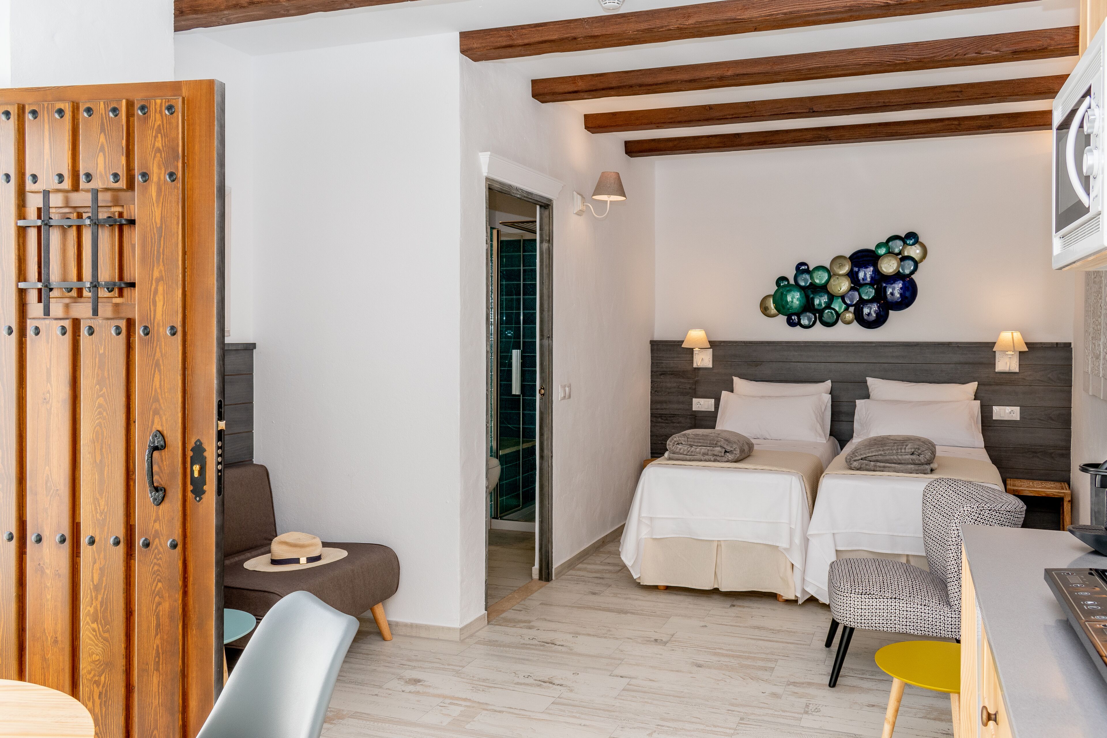 Habitación de hotel con dos camas, un armario de madera, una zona de estar con un sombrero y una obra de arte en la pared.