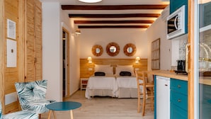 A compact room with a bed, two bedside tables, a small table, and a kitchenette. - Casa del Patio - Boutique Apartments (Estepona)