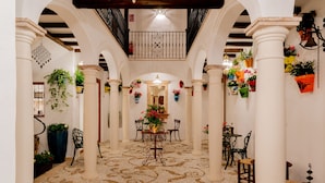 A spacious corridor with white columns, a patterned floor, and a central table with chairs. - Casa del Patio - Boutique Apartments (Estepona)