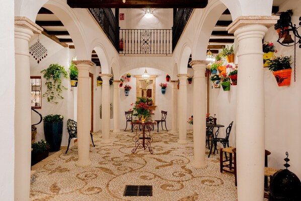 A spacious corridor with white columns, a patterned floor, and a central table with chairs.