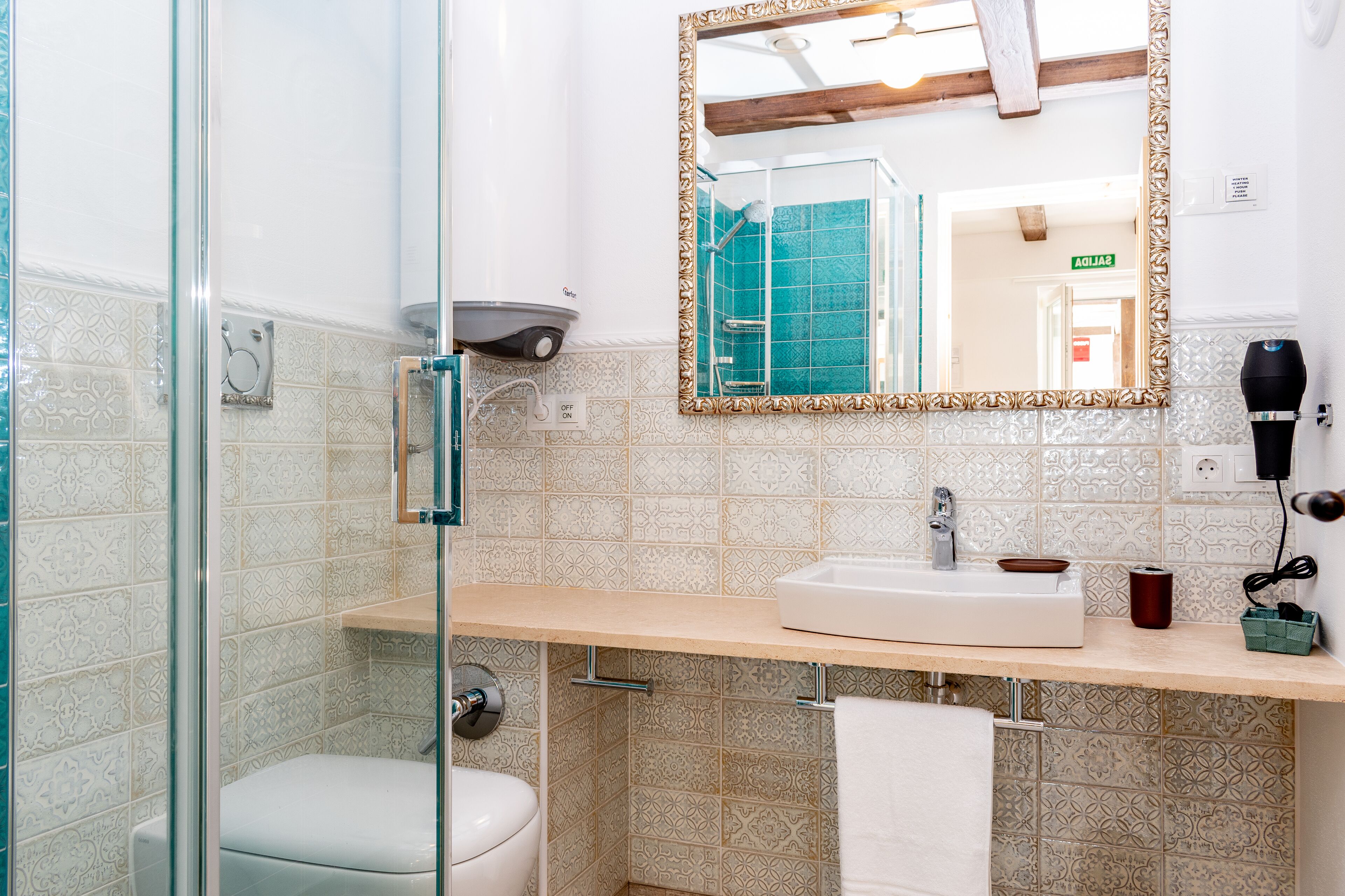 A bathroom with a glass shower enclosure, a sink with a mirror, and a towel hanging on the wall.