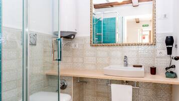 A bathroom with a glass shower enclosure, a sink with a mirror, and a towel hanging on the wall.