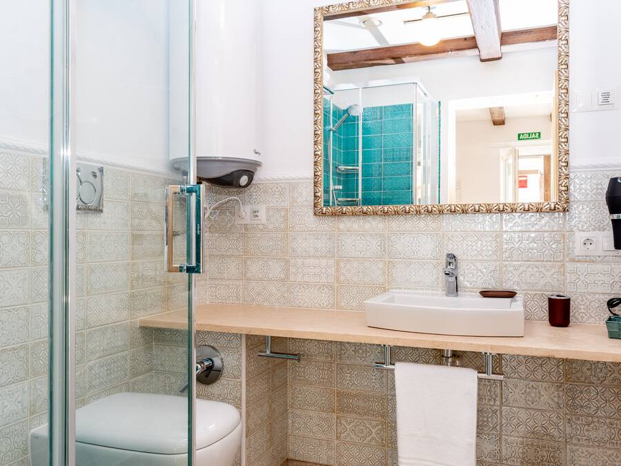 A bathroom with a glass shower enclosure, a sink with a mirror, and a towel hanging on the wall.