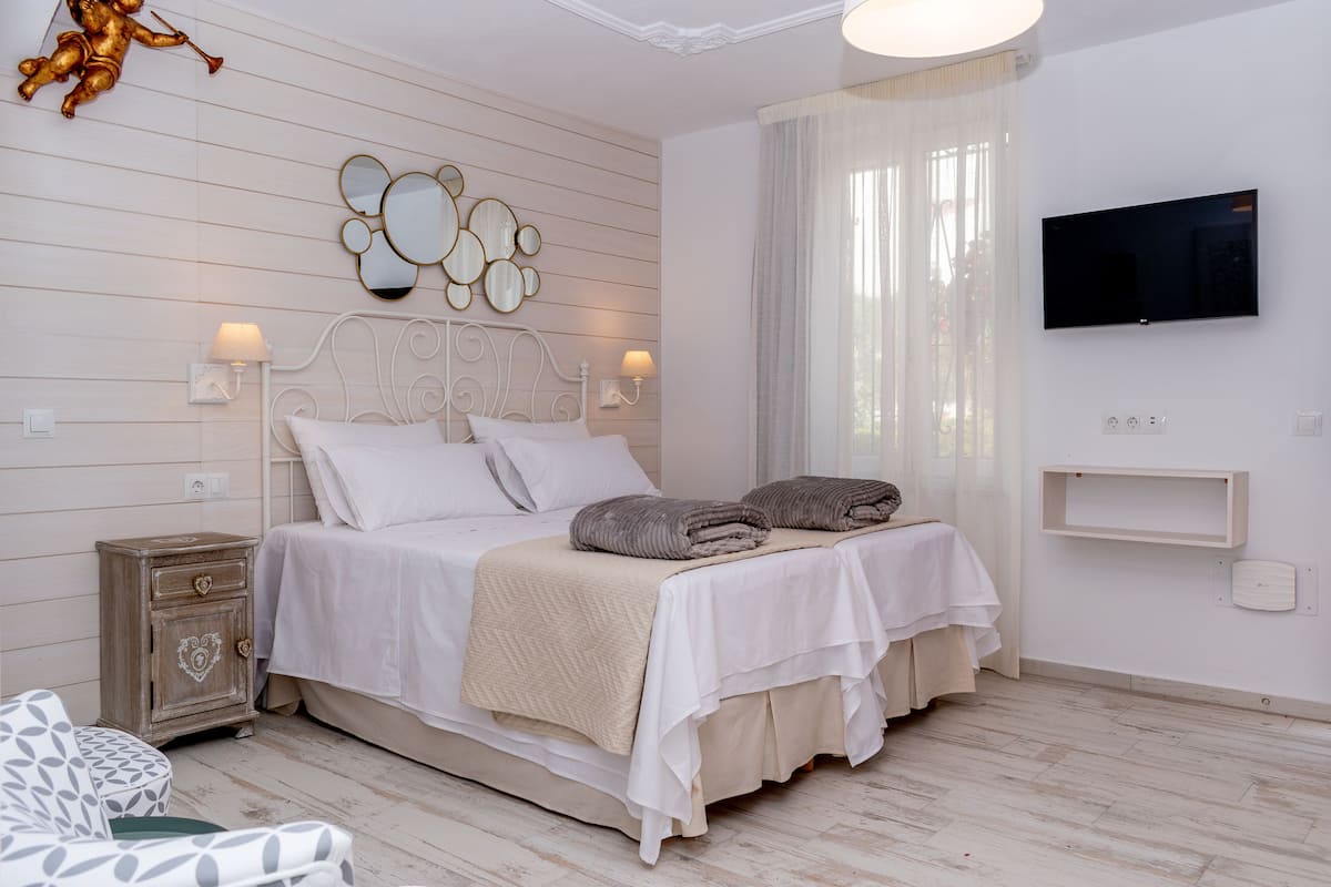 A neatly arranged bedroom with a bed, bedside lamps, a TV, and a decorative mirror on the wall.