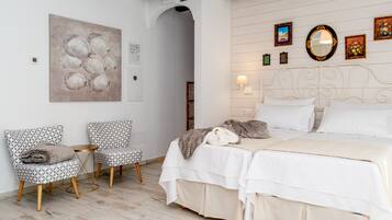 Un dormitorio con una cama, dos sillones estampados, una mesita y una obra de arte en la pared.