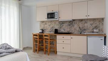 Cocina compacta con microondas, un lavamanos y un refrigerador pequeño. Hay dos sillas de madera y una mesa pequeña.