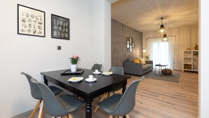 A modern living room with a dining area, featuring a dark wooden dining table, grey chairs, a grey sofa, and a grey armchair. There are framed botanical prints on the wall and a pendant light above the sofa. - Villa LuiSole - Apartment °1 with heated saltwater pool, family-friendly (Krk)