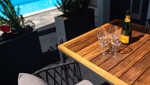 A wooden table with a bottle of champagne and three glasses, set outdoors with a pool in the background. - Villa LuiSole - Apartment °1 with heated saltwater pool, family-friendly (Krk)