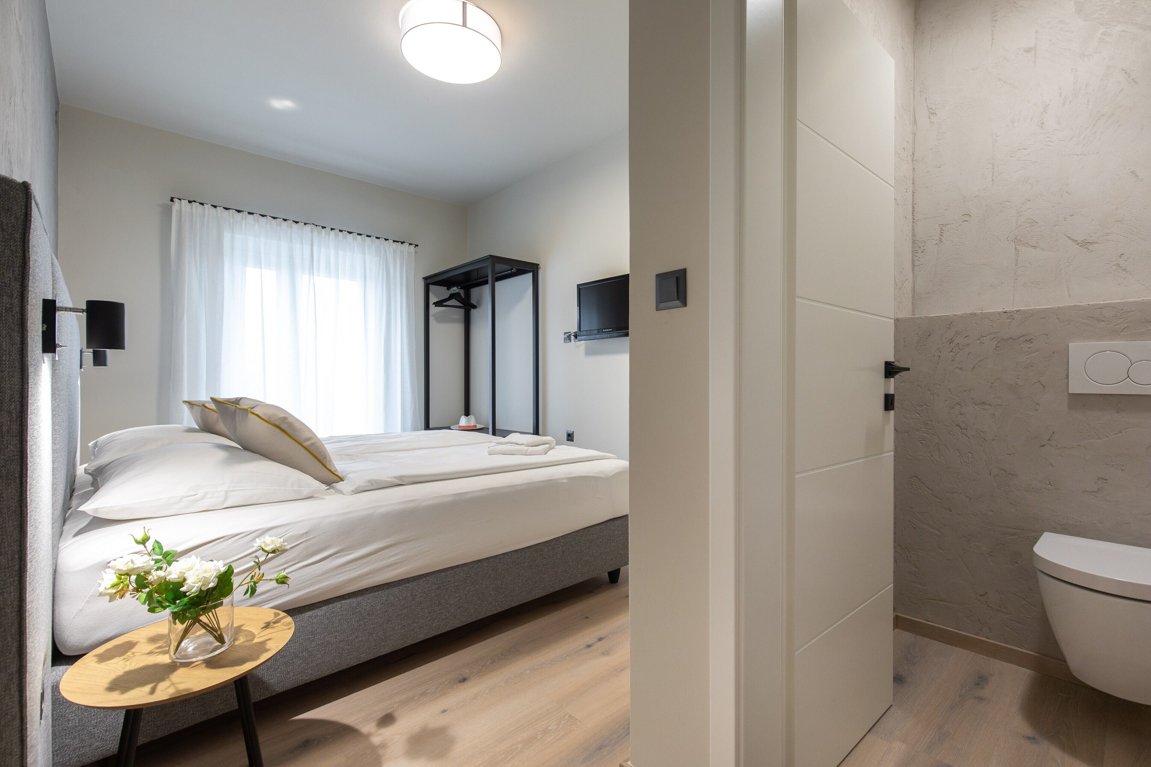 A modern bedroom with a bed, bedside table, and a bathroom with a toilet and shower.