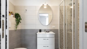 A modern bathroom with a toilet, a sink with a mirror, and a shower area.