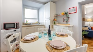A modern kitchen with a built-in microwave, a washing machine, and a dining area set for four with a table, chairs, and blue glassware.