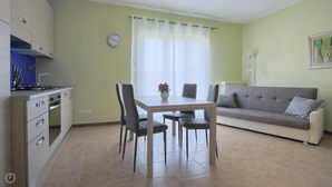 Una sala de estar moderna con una mesa de comedor, sillas, un sofá y una zona de cocina con armarios y un reloj.