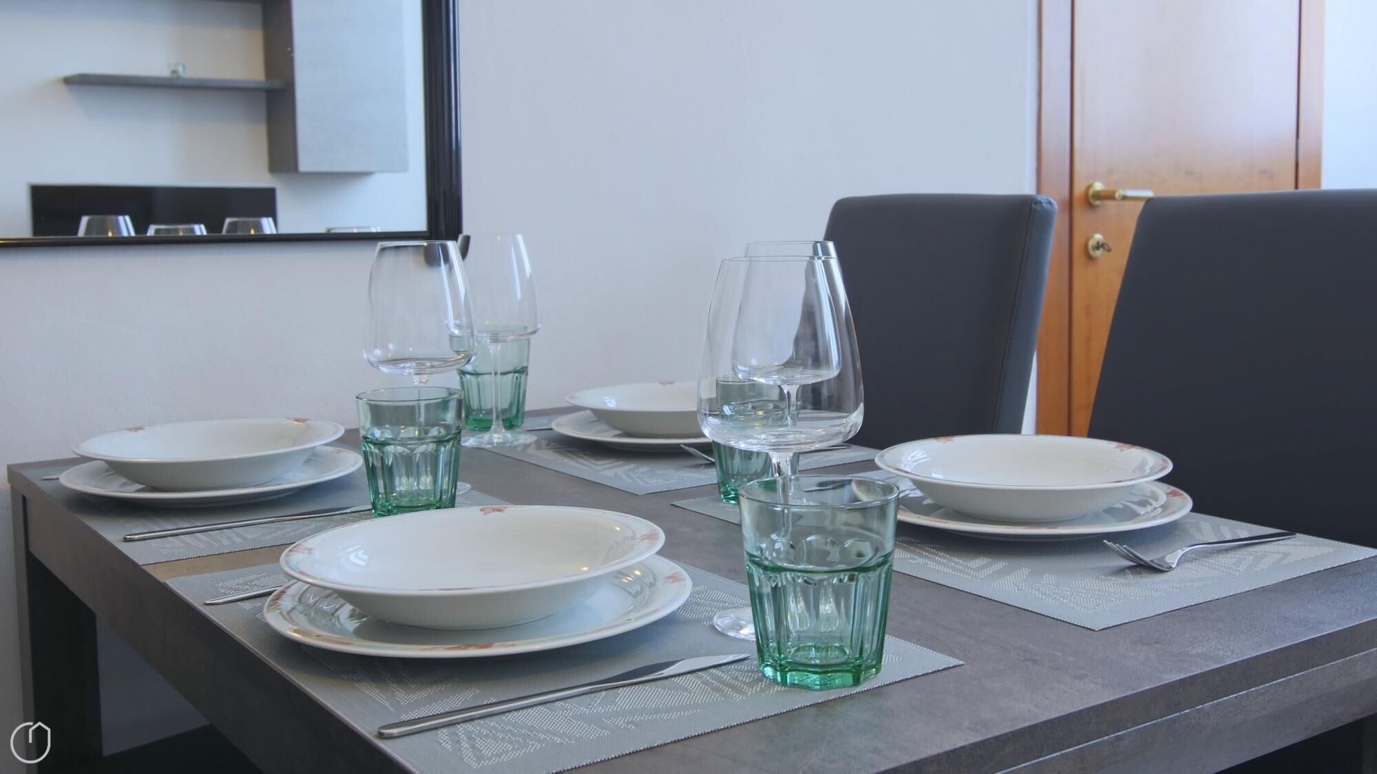 A dining table set with plates, glasses, and cutlery, with a mirror and a door in the background.