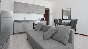 Eine moderne Küche mit grauen Schränken, einer Mikrowelle und einem Herd. Im Wohnbereich befindet sich eine graue Couch mit Kissen sowie ein Esstisch mit Stühlen.