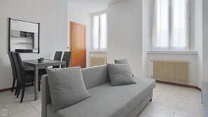 Ein modernes Wohnzimmer mit grauem Sofa, einem Esstisch mit Stühlen, einer Holztür und einem Heizkörper.