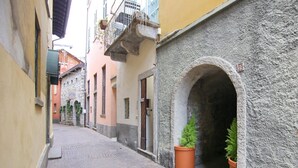 A narrow cobblestone street with historic buildings, an archway, and potted plants. - Bartolomeo de Benz - Torno (Torno)