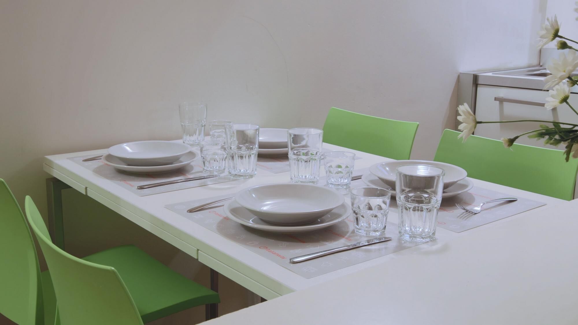 A dining table set with plates, glasses, and cutlery, surrounded by green chairs.