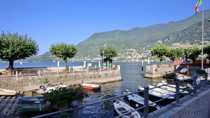 A waterfront marina with boats docked, trees, and a mountainous backdrop.