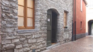A stone building with a wooden-framed window and a door, a small window with a plant, and a red wall with a window.